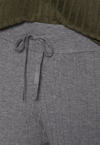 Pantalon de survêtement gris côtelé avec un cordon de serrage à la taille. Le tissu semble doux, présentant une texture subtile et des lignes verticales.