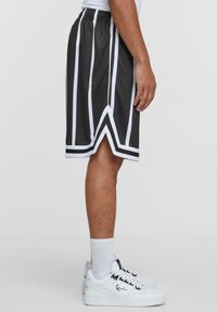 Svarta träningsshorts med vita vertikala ränder, midja med dragsnodd och V-formad nederkant; bärs med vita sneakers och ankelsockor.