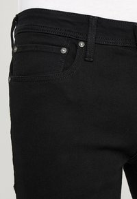 Black denim jeans featuring a classic five-pocket design, silver hardware accents, and contrasting stitching detail along the seams.