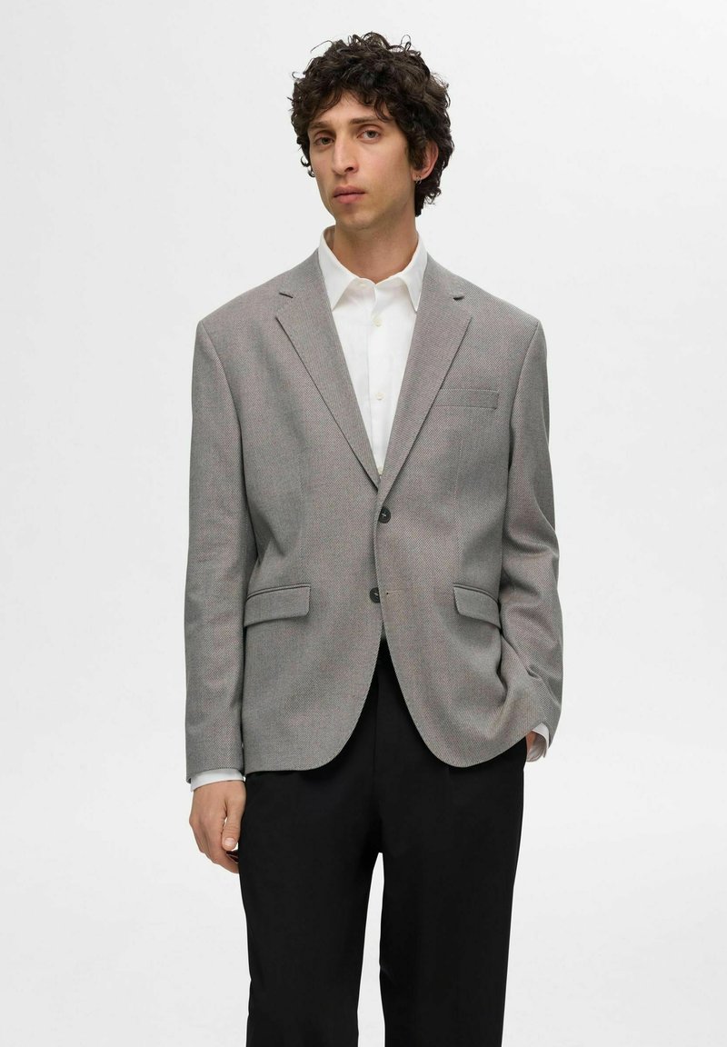 Grå blazer med strukturerad yta, enkelknäppsdesign, slagkragar, två framfickor och klassisk knäppning. Vit skjorta under.
