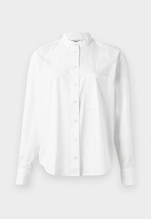 Hvit skjorte med lange ermer og ståkrage, med knappestolpe og brystlomme. Laget av lett stoff med glatt tekstur.