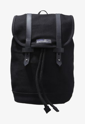 Zaino in tela nera con spallacci in pelle, chiusura a corda e forma rettangolare. Presenta una patch con logo sulla parte anteriore.