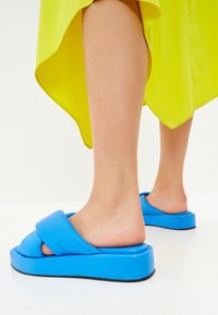 Modré platformové sandály s širokým designem popruhů. Vyrobené z měkkého materiálu, s texturovanou podešví a mírným podpatkem pro větší výšku.