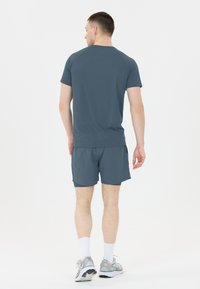 Miestenský atletický outfit v tmavosivej farbe, ktorý pozostáva z trička s krátkym rukávom a zodpovedajúcich šortiek, vyrobený z ľahkého materiálu s hladkou textúrou.