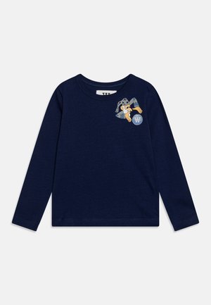 Mørkeblå langærmet skjorte med en tegneseriehund, der bærer en grå hat og rækker mod en cirkulær logo på venstre bryst.
