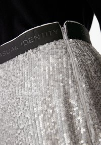 Gonna argento con paillettes e superficie testurizzata, dotata di una vita elastica nera con l'etichetta "CASUAL IDENTITY." Dettaglio con zip visibile sul lato.