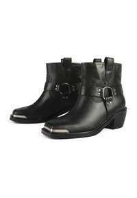 Botas de cuero negro hasta el tobillo con puntera redondeada, puntera de metal y una correa decorativa con detalles en metal. Tacón ligeramente elevado.