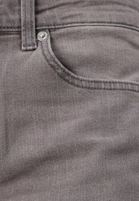 Țesătură din denim gri cu o textură subtilă în țiglă, având un buzunar frontal, bucle pentru curea și un accent cu buton metalic.