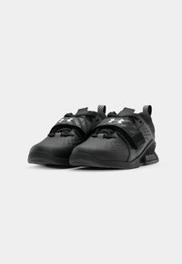 Czarne buty sportowe z teksturowaną cholewką, regulowanym paskiem i perforowanym wzorem zapewniającym wentylację. Gumowa podeszwa z lekkim obcasem.