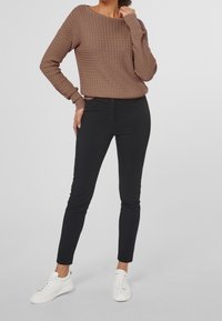 Brązowy sweter o fakturowanej strukturze, luźny, w połączeniu z czarnymi spodniami typu slim-fit i białymi sneakersami. Subtelny wzór splotu na swetrze.