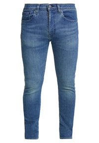 Jeans ajustados de color azul, fabricados en denim, con cinco bolsillos, cierre de botón y áreas desgastadas para un aspecto usado.