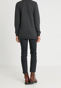 Persona che indossa un top a maniche lunghe grigio scuro, jeans skinny neri e stivaletti alla caviglia marroni con lacci, vista da dietro.