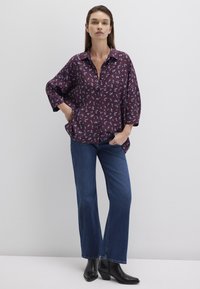 Burgundy button-up shirt with small blue floral print, loose design, paired with wide-leg blue jeans and black heeled ankle boots.