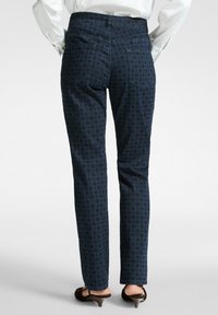 Pantalones de patrón azul marino con corte slim, que cuentan con dos bolsillos traseros y un diseño de tejido texturizado, combinados con calzado oscuro.