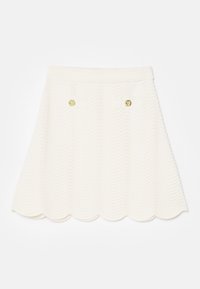 Jupe blanche texturée avec un ourlet festonné, présentant des motifs en vagues et deux poches avant ornées de boutons dorés.