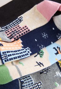Quatre paires de chaussettes à motifs exposées. Les couleurs comprennent le marine, le beige, le gris et le noir. Les motifs représentent des bâtiments, des flocons de neige et des arbres.