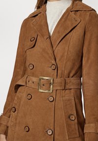 Brun dubbelknäppt kappa i mocka med skärp i midjan, stora knappar och klassisk krage. Mjuk textur med sidfickor.