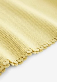 Tessuto lavorato a maglia giallo con una texture a coste, caratterizzato da un bordo ondulato. La superficie appare morbida e leggermente elastica.