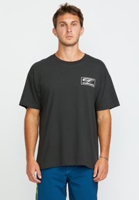 T-shirt en coton noir avec un col rond et des manches courtes. Présente un logo blanc imprimé sur la poitrine gauche. Texture lisse et coupe décontractée.