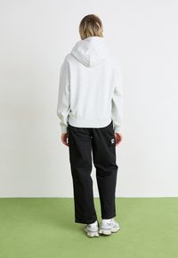 Lichtgrijze fleece hoodie met een capuchon, met ribgebreide manchetten en zoom. Gecombineerd met zwarte cargo broeken met zijzakken en een logo patch.