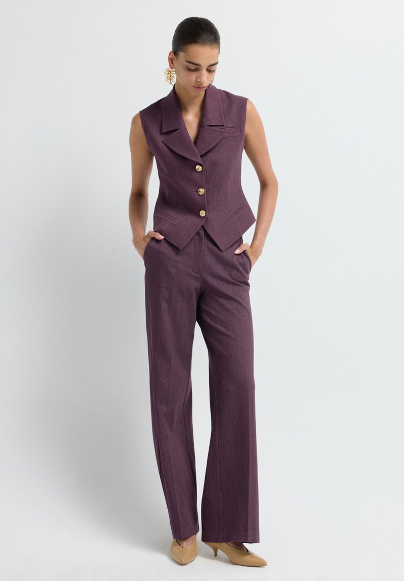 Purple sleeveless blazer with gold buttons, tailored fit, paired with matching wide-leg trousers. Smooth texture with a refined finish.