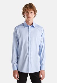 Camicia button-up a maniche lunghe di colore azzurro chiaro, realizzata in tessuto morbido, con colletto classico e sei bottoni frontali, dal taglio adattato.