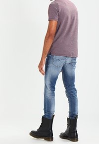 Bordowa prążkowana koszulka z krótkim rękawem i fakturowanymi ramionami, zestawiona z jasnoniebieskimi dopasowanymi jeansami i czarnymi sznurowanymi botkami wojskowymi.