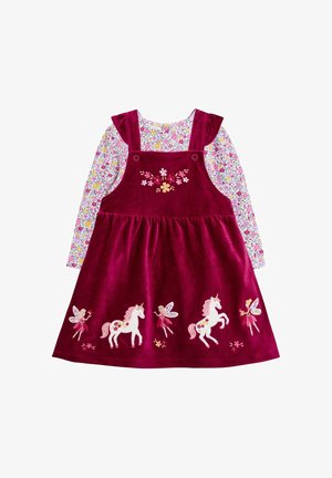 Burgundi corduroy pántos ruha hímzett egyszarvúkkal és tündérekkel, egy hosszú ujjú virágmintás ing felett, mely pink, sárga és lila virágokkal díszített.