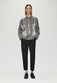 Zilverkleurig metallic lange mouwen top met een ronde halslijn en een sleutelgatdetail, gecombineerd met zwarte tapered trousers en zwarte schoenen.