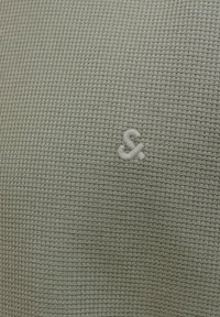 Gros plan sur un tissu tricoté en forme de gaufre de couleur vert clair avec un petit symbole esperluette brodé au centre.