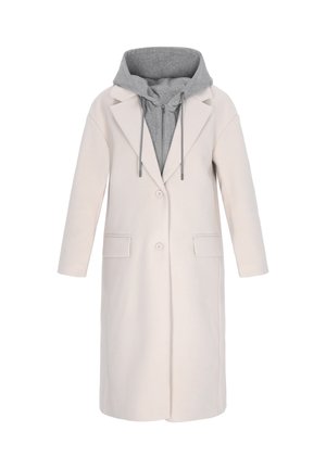 Pikk heledat beež mantel, millel on keha järgiv lõige, suured klapid ja kaks esi-taskut; all on hall kapuutsiga särk, millel on nöörid.