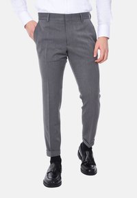 Pantaloni eleganti grigi, su misura, con una texture liscia, caratterizzati da una vestibilità slim, tasche laterali e un orlo con risvolto. Abbinati a mocassini neri.
