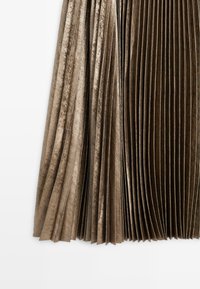 Gonna plissettata in una tonalità bronzo metallico, realizzata in tessuto testurizzato, che presenta pieghe verticali e una finitura liscia.