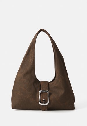 Sac en tissu marron avec une forme arrondie et une seule sangle pour l'épaule. Présente un accent de boucle en argent proéminent à l'avant. Texture lisse.