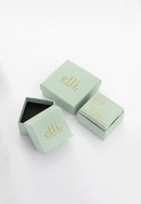 Sekskantede mintgrønne kasser med guldtryk, hvoraf den ene er åben og afslører et sort indre. Har et lille logo og brandingdetaljer.