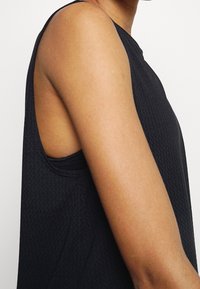 Zwarte mouwloze top met een textuur gebreid design. Het heeft een ronde halslijn en zijsplitten voor bewegingsvrijheid.