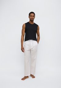 Μαύρο αμάνικο τοπ σε συνδυασμό με ανοιχτό μπεζ, φαρδιές παντελόνες με συγκεντρωμένη μέση. Το ύφασμα φαίνεται λείο και ελαφρύ.