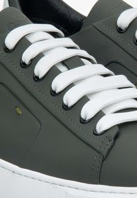 Tmavě zelené syntetické tenisky s bílými tkaničkami, obsahující černé očnice, texturovaný svršek a bílou gumovou podrážku. Přítomný malý zelený akcent.