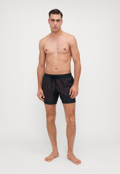 Pantaloni scurți de baie negri cu litere roșii imprimate, talie elastică și șnur. Material ușor, textură netedă, potriviți pentru plajă.