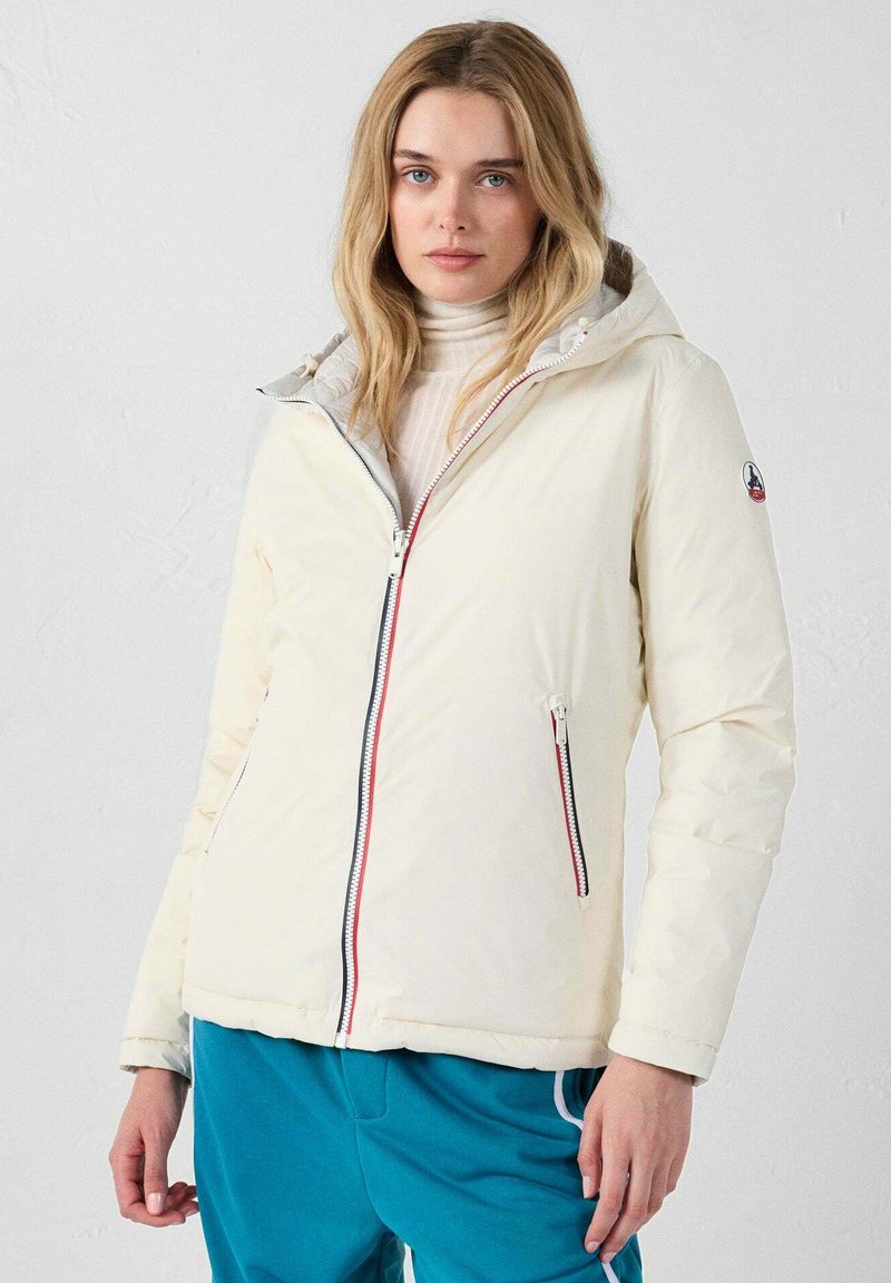 Parka de plumas de color crema claro con capucha, dos bolsillos con cremallera y cremalleras en contraste rojas y azules. Textura suave y brillante.