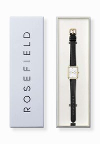 Rosefield-Uhr in einer Box, mit einem quadratischen weißen Zifferblatt, goldenen Akzenten und einem schwarzen Lederarmband mit Naht und Schnallen-Details.