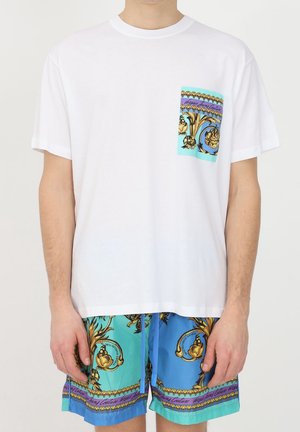 Man wearing white t-shirt with colorful baroque pattern pocket paired with matching blue and turquoise patterned shorts with drawstring.