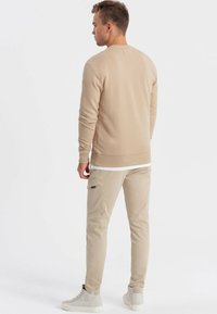 Sweatshirt beige a maglia con polsini e orlo a costine, abbinato a pantaloni cargo beige chiaro con tasche laterali. Sneakers chiare completano l'outfit.