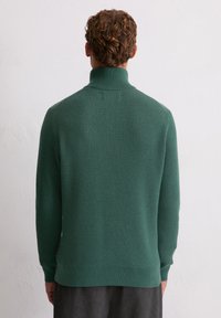 Pull vert côtelé avec un col haut et des manches longues, présentant un motif de tricot texturé et une silhouette ajustée.