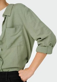 Lichtgroene button-up shirt gemaakt van textuurstof, met een borstzak en opgerolde mouwen met knoopaccenten.