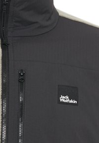 Schwarze Zip-Jacke mit einem grauen Fleece-Einsatz, ausgestattet mit einem strukturierten Stoff, kontrastierenden Reißverschlüssen und einem quadratischen Logo-Patch mit "Jack Wolfskin".