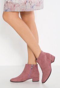 Stivali alla caviglia in camoscio viola con tacco basso a blocco, dotati di cerniera laterale e texture liscia, completati da un design con punta affusolata.