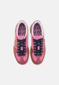 Růžové semišové tenisky s námořnickými tkaničkami a gumovou podešví. Vnitřek má geometrický vzor v růžové a námořnické barvě. Zlaté prvky loga.