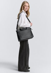 Sac en cuir noir au design structuré, avec des poignées supérieures et une bandoulière réglable. Texture lisse avec des détails en matériel minimaux.