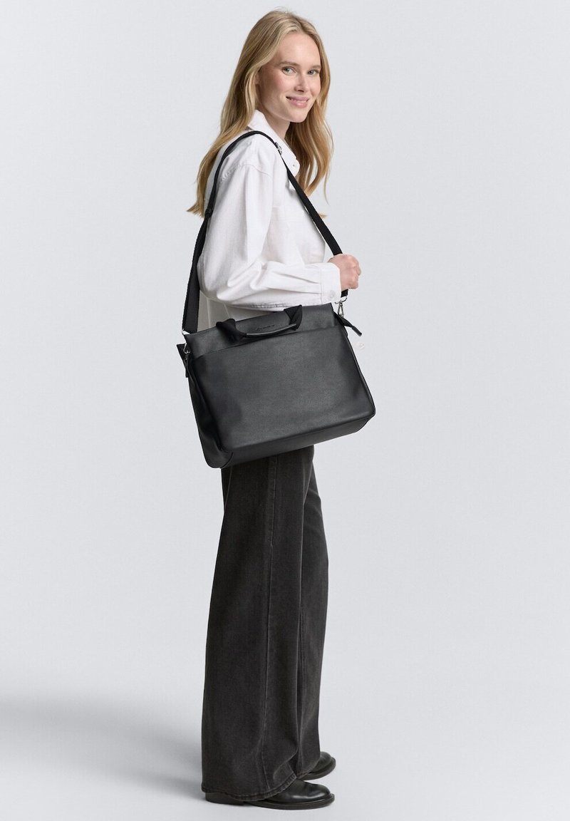 Sac en cuir noir au design structuré, avec des poignées supérieures et une bandoulière réglable. Texture lisse avec des détails en matériel minimaux.